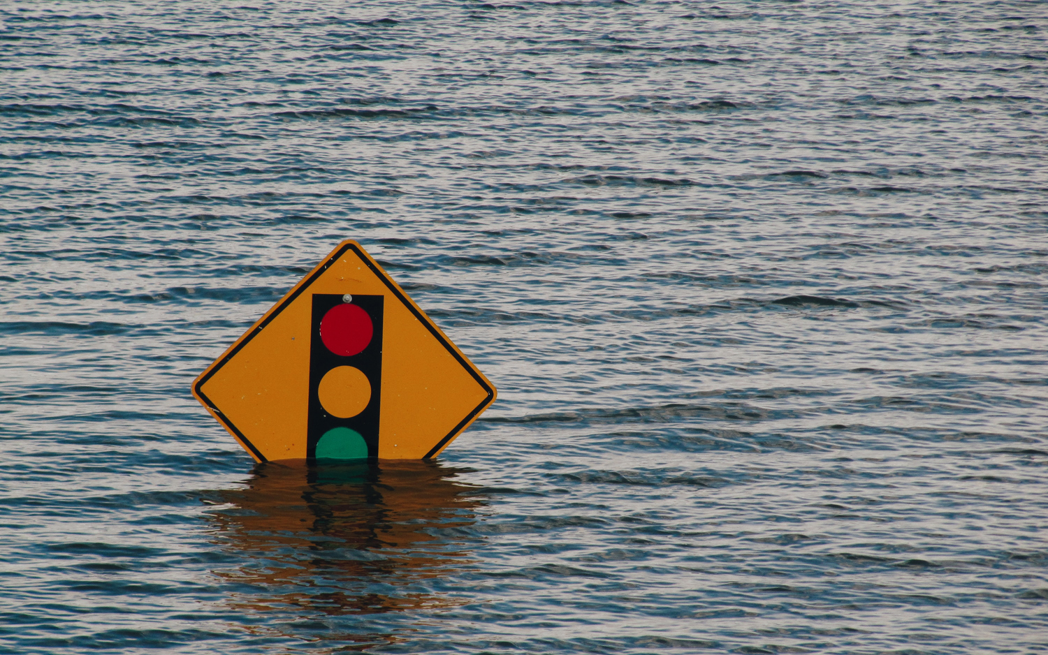 A street sign mostly submerged under water due to flooding as an image for Climate Change. Photo by Kelly Sikkema on Unsplash