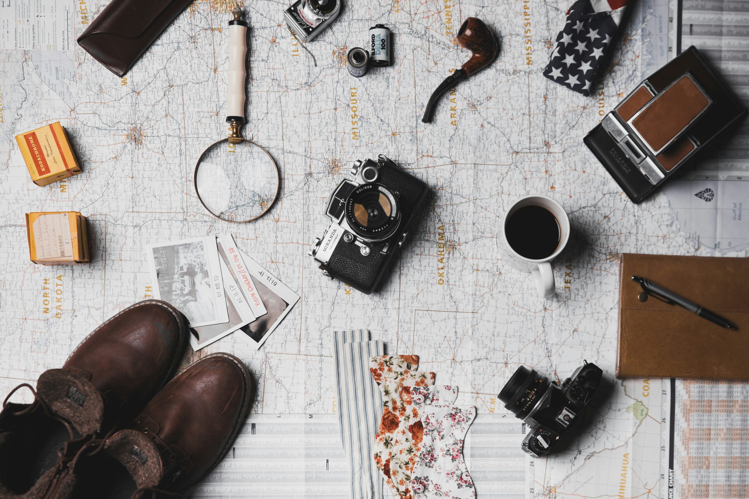 A table full of vintage travel gear like a camera, boots, magnifying glasses... Photo by ian dooley on Unsplash